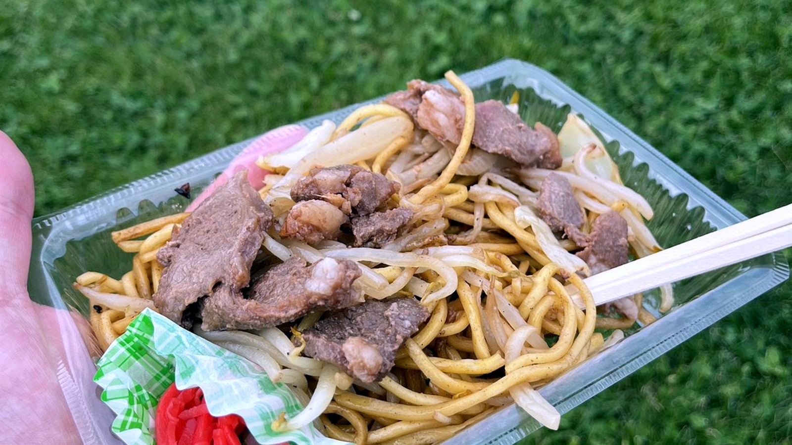 芝生を背景に手に持ったパック入りの焼きそば