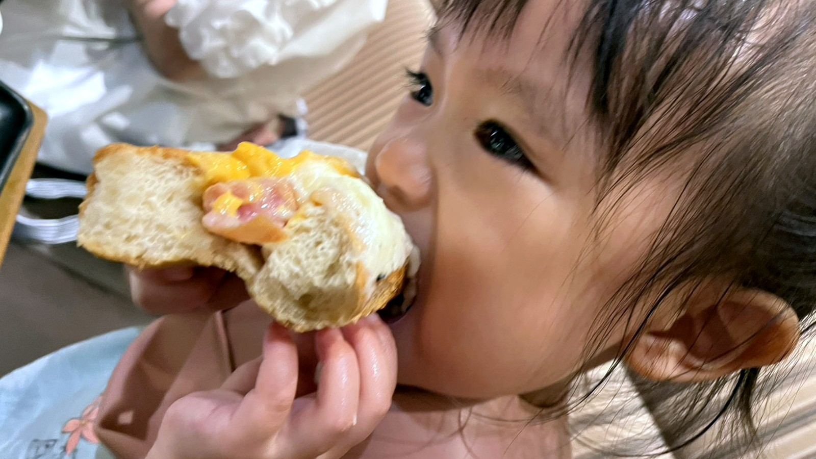惣菜パンを大きな口で頬張る小さな女の子